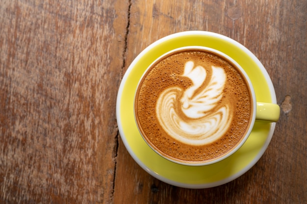 Top view of Latte coffee or cappuccino coffee in yellow cup with swan latte art on wooden table.