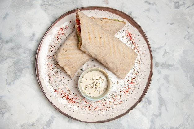 Photo top view of lavash wrap and yogurt in a small bowl on a plate on stained white surface