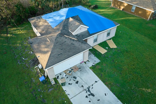 Top view of leaking house roof covered with protective tarp sheets against rain water leaks until replacement of asphalt shingles Damage of building rooftop as aftermath of hurricane Ian in Florida