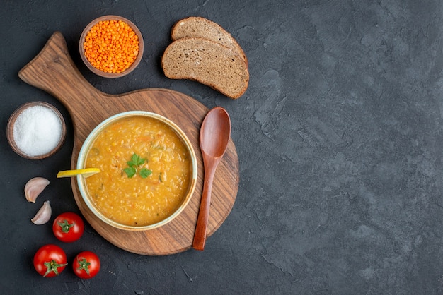 Top view lentil soup with salt raw lentils and dark bread loaves on dark surface