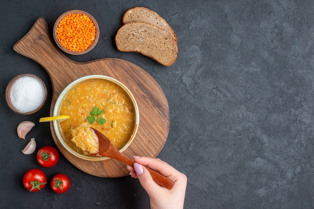 Top view lentil soup with salt tomatoes and dark bread loaves on dark surface
