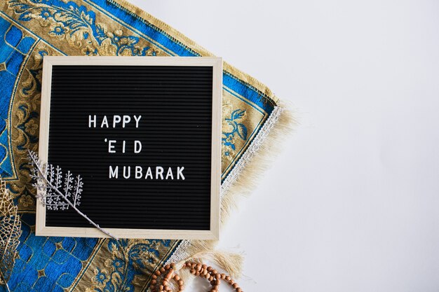 Top view of letter board says Happy Eid Mubarak on the prayer mat with copy space