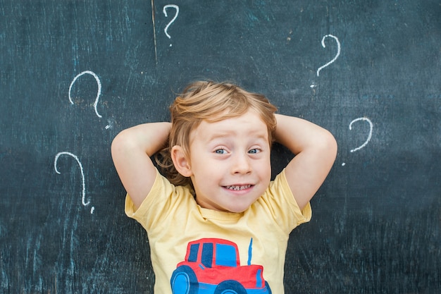 Top view of a little blond kid boy with question mark on blackboard