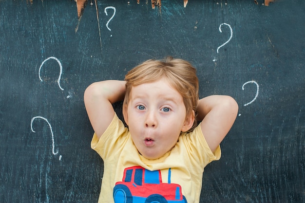 Photo top view of a little blond kid boy with question mark on blackboard