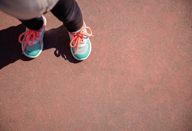 Top view of little girl legs with sneakers and black leggins over a garnet floor outdoors