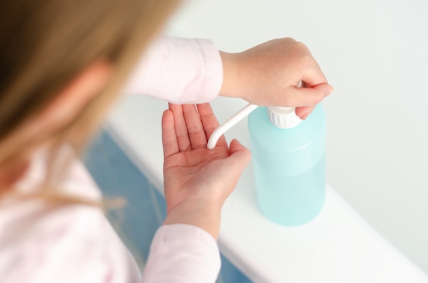 Vista dall'alto di una bambina che utilizza disinfettante disinfettante per le mani in tempi di pandemia di virus globale