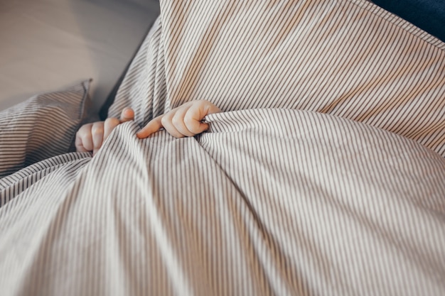 Photo top view of little kid in bed covering his face with blanket. morning