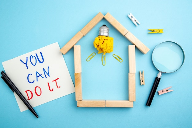 Top view lupa idealight bulb in house shaped wood blocks you\
can do it written on paper pen small clothespins on blue\
background