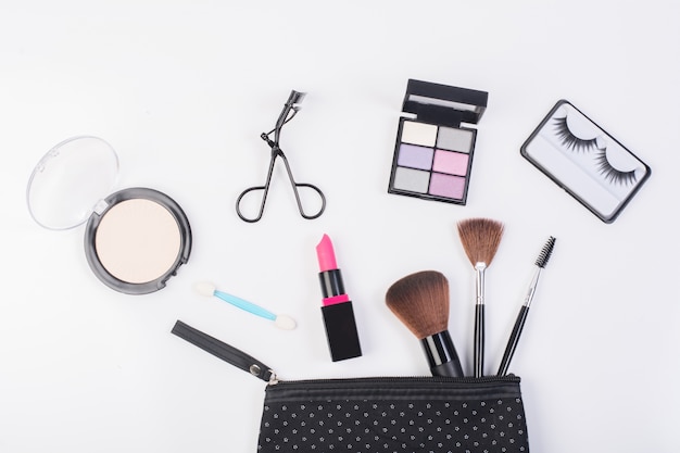 Top view of a make up bag, with cosmetic beauty products spilling out onto a  white background.