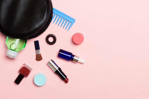 Top view of make up products fallen out of cosmetics bag on pink background. Cosmetic concept with space for your design