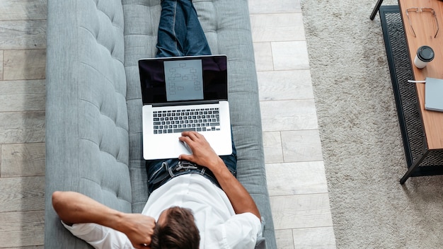 Top view. male freelancer is working on a laptop while lying on the couch . domestic life.