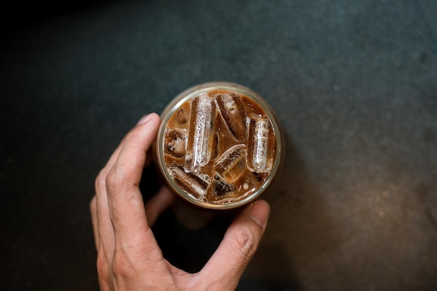 Top view of male hand holding a takeout iced coffee on black table