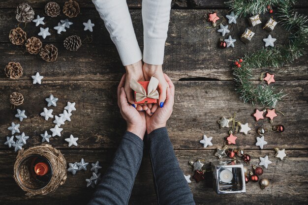 Top view of a male hands cupping female hands holding small red holiday gift box