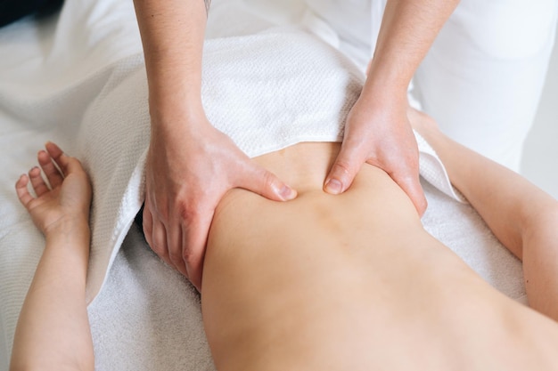 Top view of male masseur massaging lower back of young woman lying on massage table at spa salon