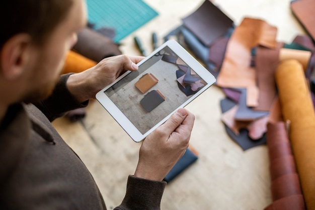 Photo top view male tanner use tablet at leather workshop craftsman creating online advertising promotion