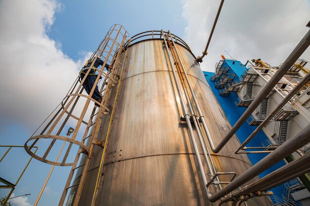 Photo top view male worker climbs up the ladder inspection stainless tank work at height