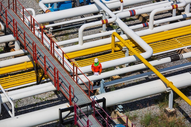 Top view male worker inspection at steel long pipes and pipe\
elbow valve in station oil factory during refinery valve of visual\
check record pipeline oil