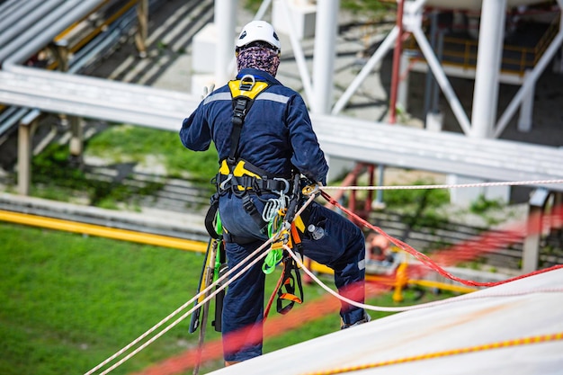 Top view male worker inspection wearing safety first harness\
rope safety line working at a high place on tank roof spherical\
gas