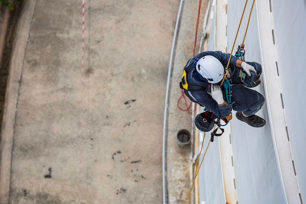 Ispezione del lavoratore maschio vista dall'alto che indossa la prima linea di sicurezza della fune dell'imbracatura di sicurezza che lavora in un punto alto sul tetto del serbatoio sferico