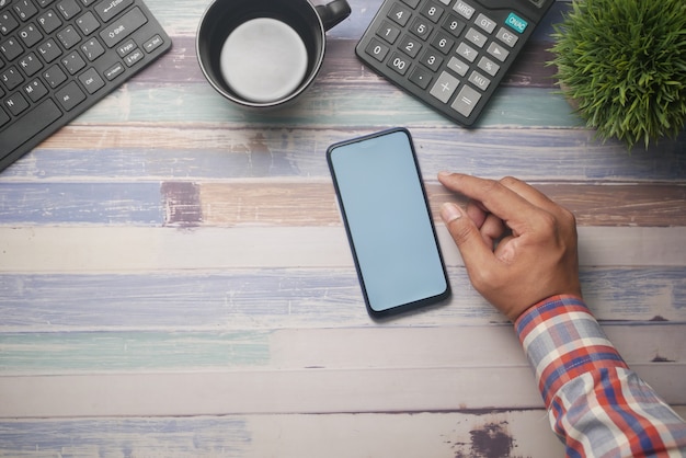 Vista dall'alto della mano dell'uomo utilizzando lo smartphone sulla scrivania dell'ufficio