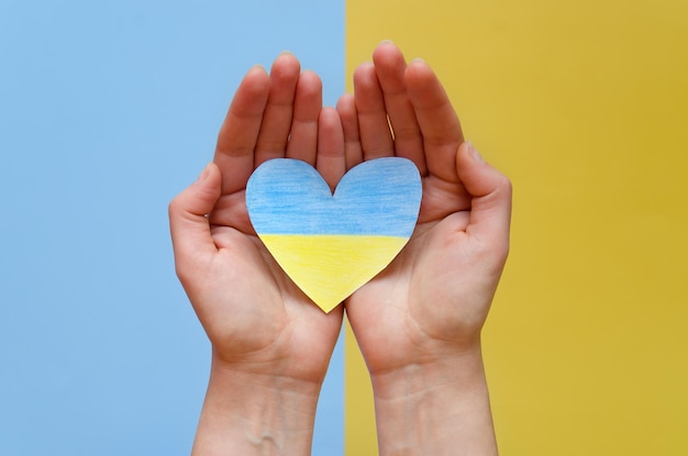 Top view. man hands holding Ukraine flag painted heart isolated on yellow, blue background. Support