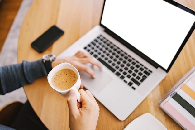 Top view of a man holding a fresh cup of coffee and typing on a keyboard at home