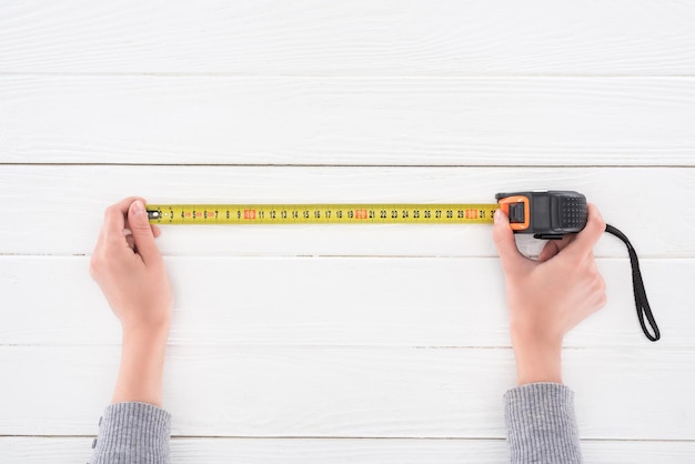 Top view of man holding industrial measuring tape on white wooden surface