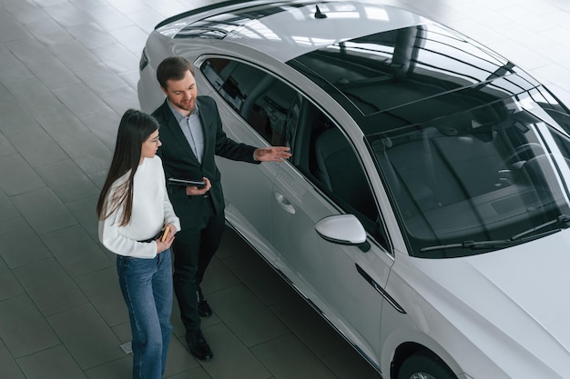 top view man is showing the new automobile to the woman customer in the car dealership