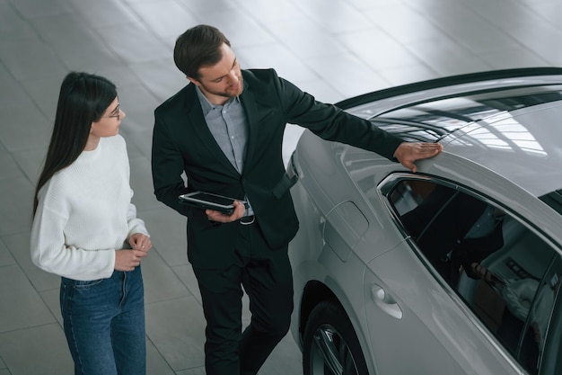 Photo top view man is showing the new automobile to the woman customer in the car dealership