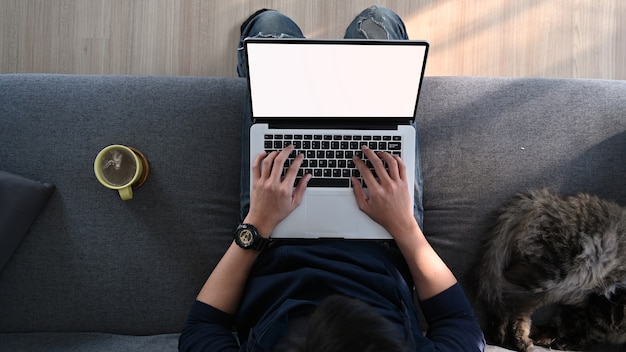 Top view a man typing mockup laptop computer with empty screen on sofa home.