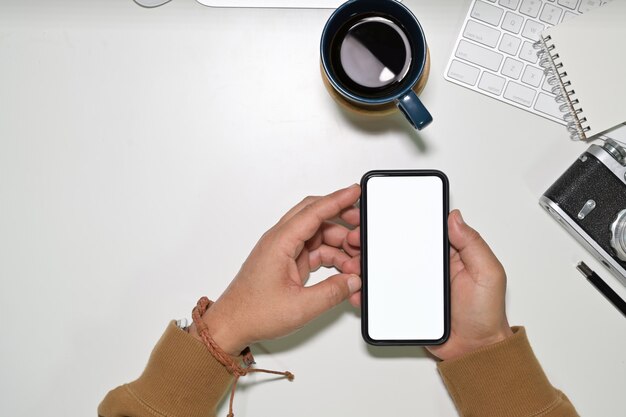 Top view man using a mobile smartphone over a workspace desk, blank screen mobile phone