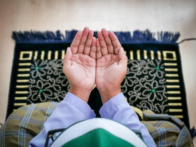Photo top view man with praying hands sit on praying mat.