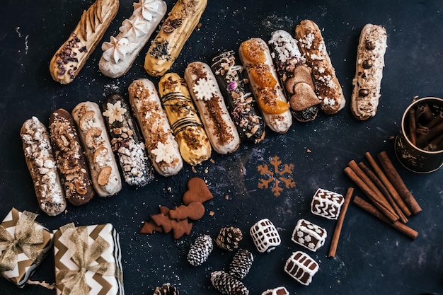 Top view of many Traditional French dessert eclairs composed with a gift box cinnamon gingerbread on a dark table Shot in a cafe or restaurant