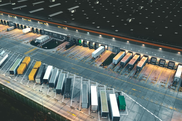 Вид сверху на множество трейлеров и контейнеров возле логистического склада вечером
