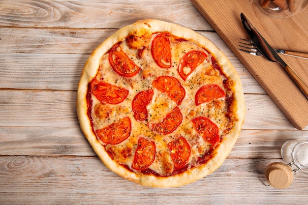 Top view on margherita pizza with tomatoes on the wooden background