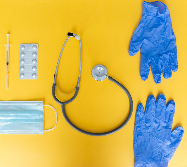 Foto vista superiore del medico dello stetoscopio, della siringa, dei guanti in lattice, della maschera e delle pillole su sfondo giallo