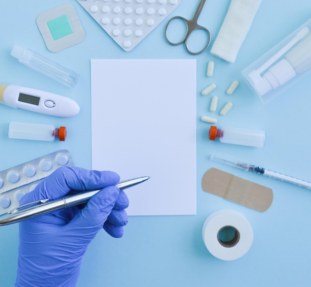 Vista dall'alto delle forniture mediche pillole pritspatch vaccini che giacciono su uno sfondo blu la mano di un medico in un guanto medico che tiene una penna quarantena epidemica concetto sano