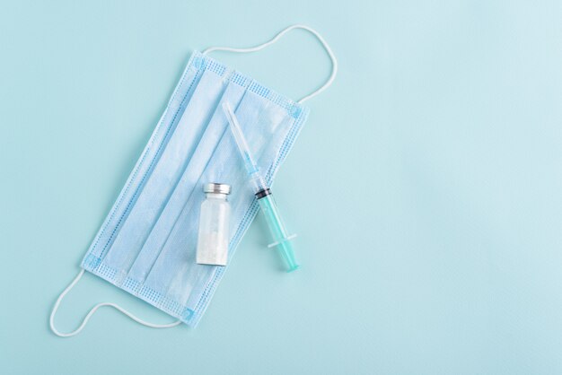 Top view medical syringe, ampoule, medical mask on blue background, vaccination, inoculation concept, copy space