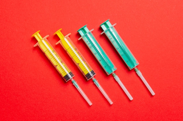 Top view of medical syringes with needles at red background with copy space. Injection treatment concept.