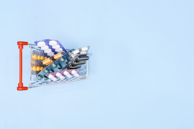Top view of medicines in shop trolley on a blue background with copy space.