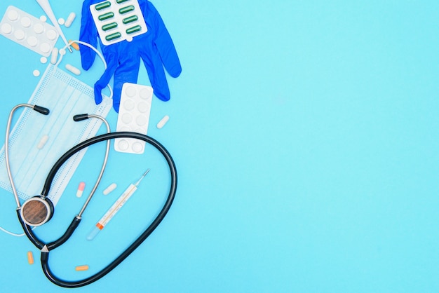 Top view of medicines, work tools and accessories doctor, nurse. Medical set - Tablets, thermometer, syringe, ampoules, adhesive plaster and statoscope on a blue background. Flat lay