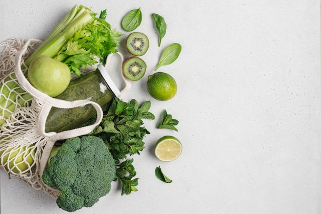 Top view of mesh shopping bag with organic green eco fruits vegetables and green smoothie in bottle