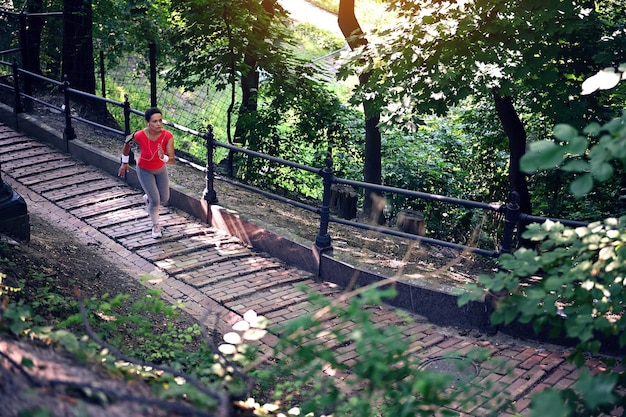 Top view of a middleaged sportswoman running on stairs along railing in forest park Cardio workout jog active and healthy lifestyle concept