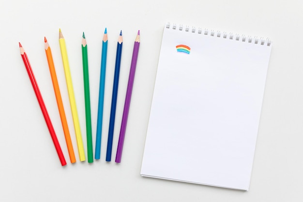 Top view Minimal design of open Notebook with colored pencils of rainbow colors on white background with blank space Flat lay