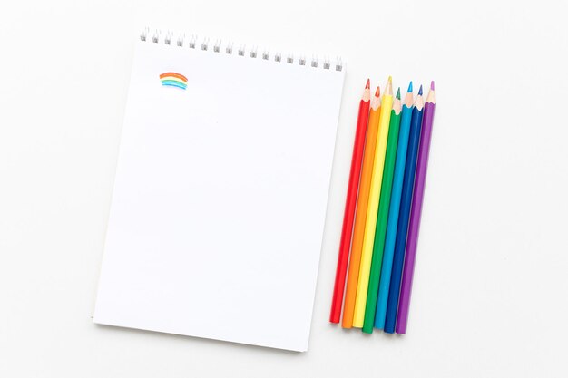 Top view Minimal design of open Notebook with colored pencils of rainbow colors on white background with blank space Flat lay