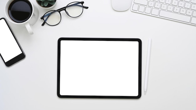 Top view of minimal office desk with mock up digital tablet with blank screen, smart phone, keyboard and glasses on white background.