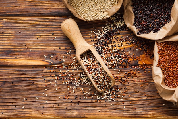 Top view of Mix of quinoa seeds - Chenopodium quinoa in the wooden scoop scatterd on the wooden table