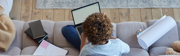 Top view of mixed race teen girl browsing the internet using laptop while sitting on the sofa at