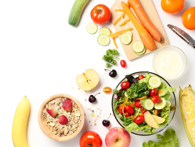 Top view of mixed vegetables salad, muesli and fresh fruits on white background