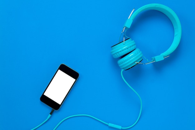 Top view mobile phone and headphones on blue background with copy space.